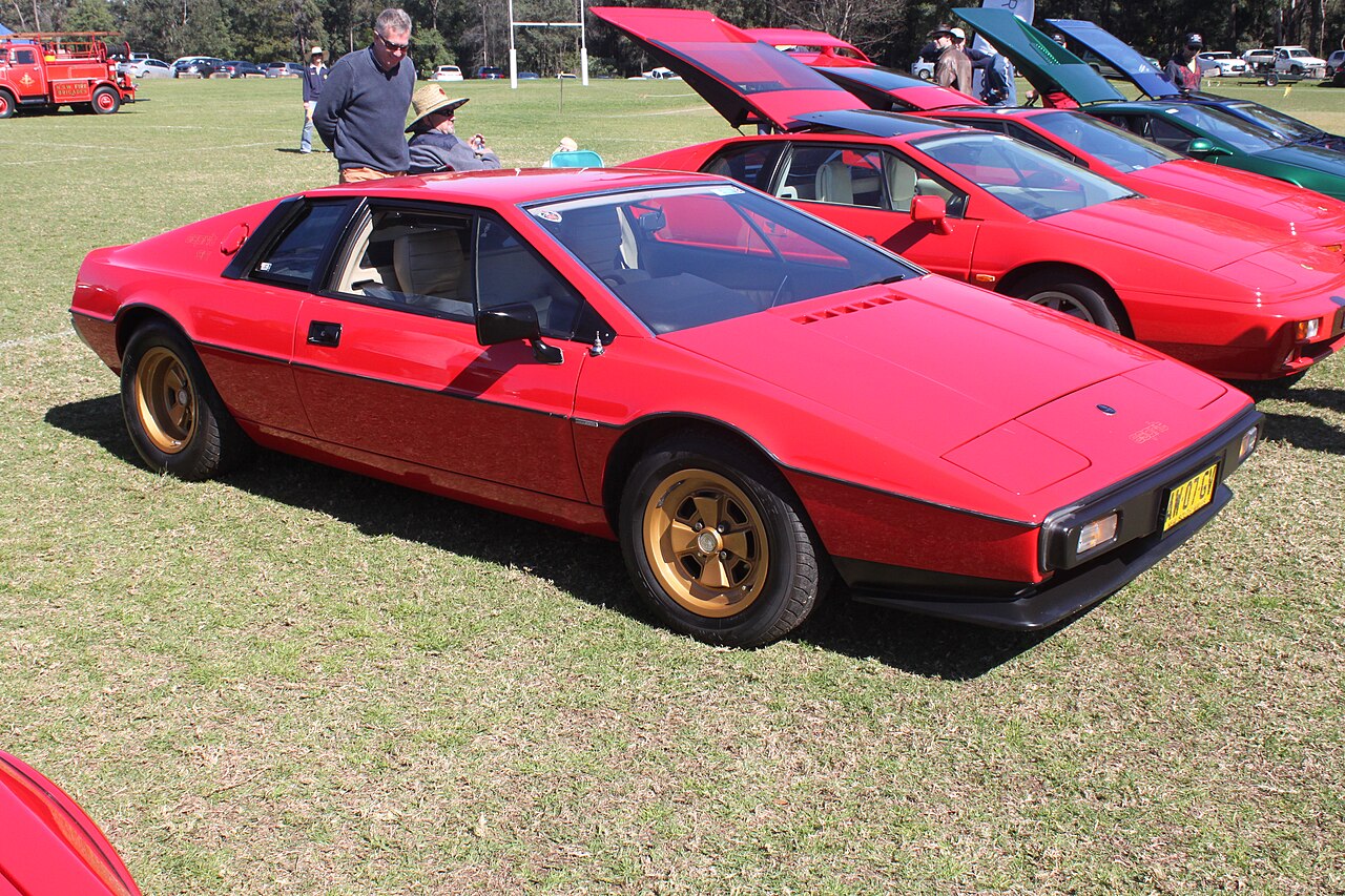 Red Lotus Esprit S2 with gold wheels, front right three-quarter view on grass at a car show, with other Esprits behind.