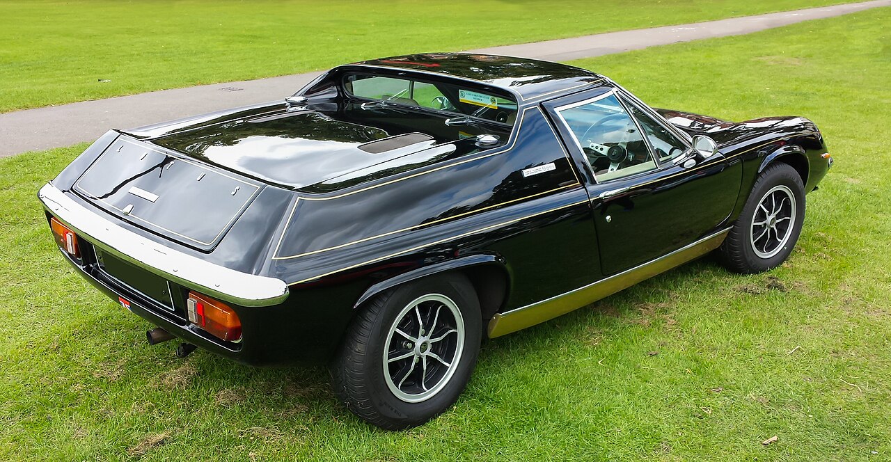 Black 1972 Lotus Europa Special with gold stripes, rear three-quarter view on grass.
