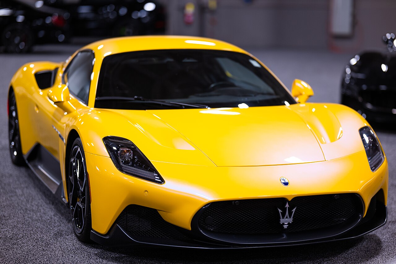 Yellow Maserati MC20 coupe, front three-quarter view on carpet at an indoor auto show.