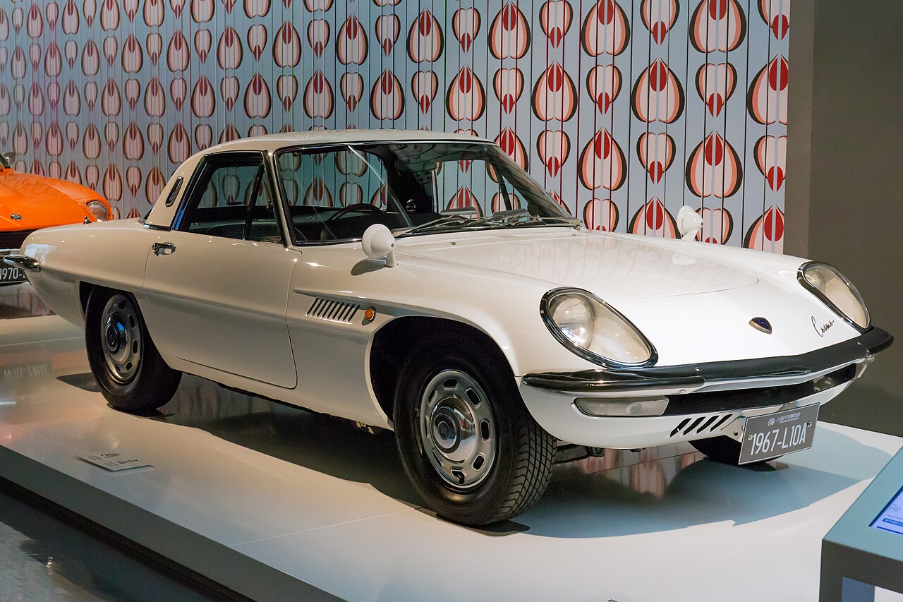 White Mazda Cosmo Sport coupe, front right three-quarter view on a display stand in a museum.