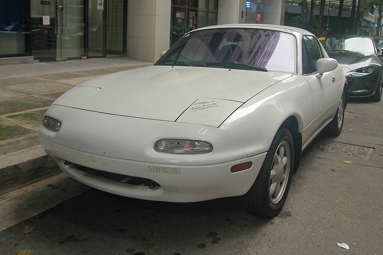 White 1991 Mazda MX-5 Miata NA with its hardtop fitted, front left three-quarter view parked on a city street.