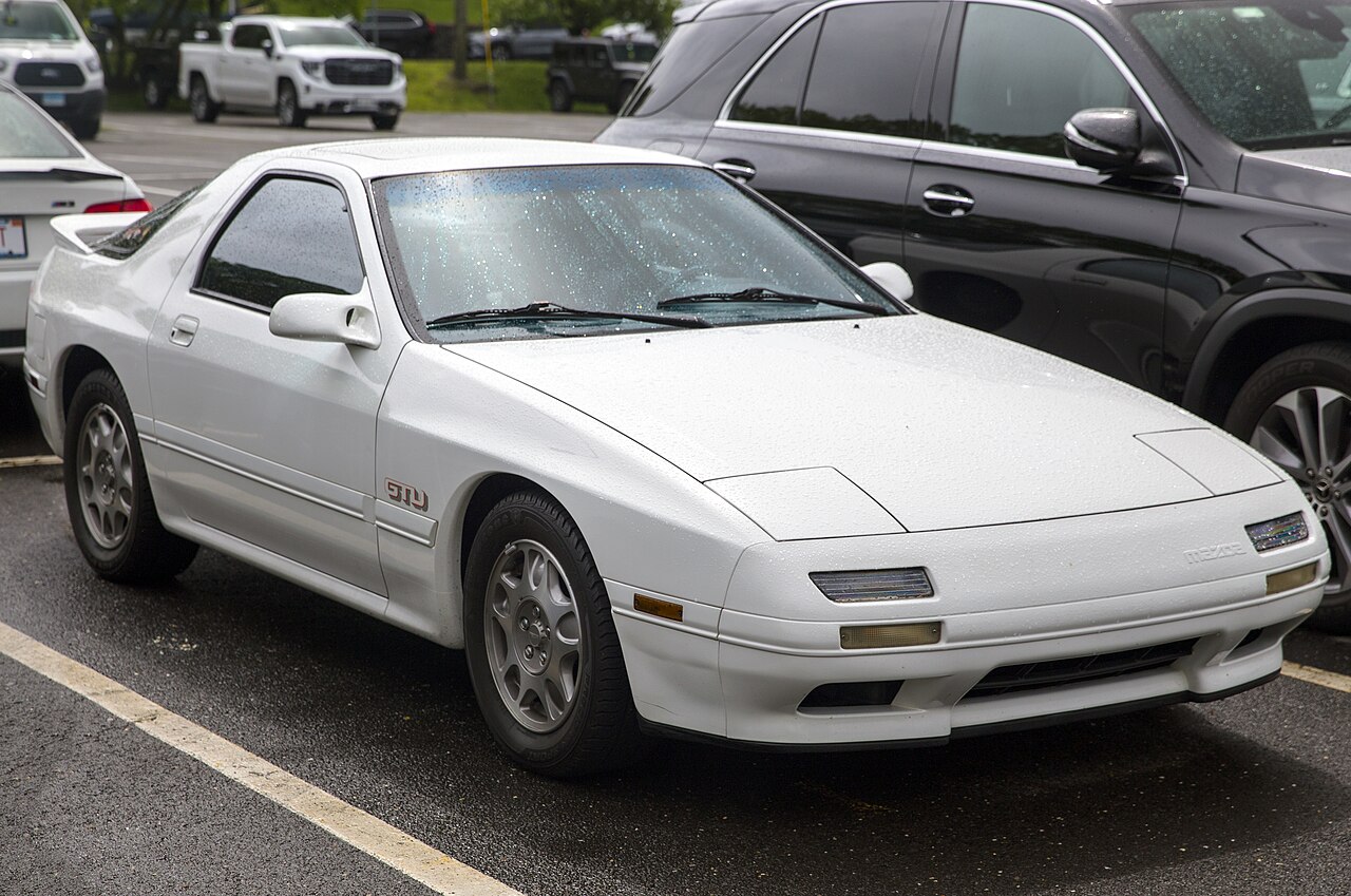 1989 Mazda RX-7 GTU in white, front three-quarter view in a wet car park.