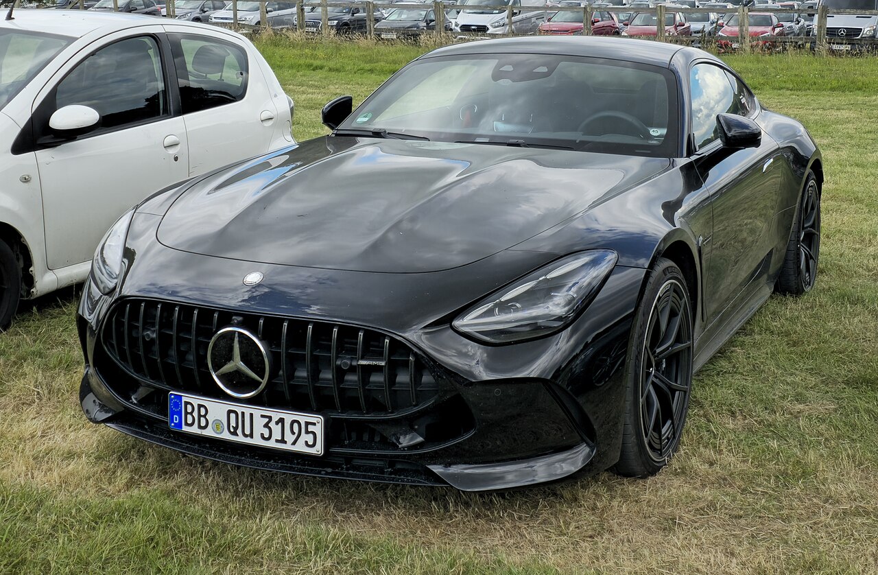 Black second-generation Mercedes-AMG GT coupe with a vertical-slat grille, front three-quarter view parked on grass beside other cars.