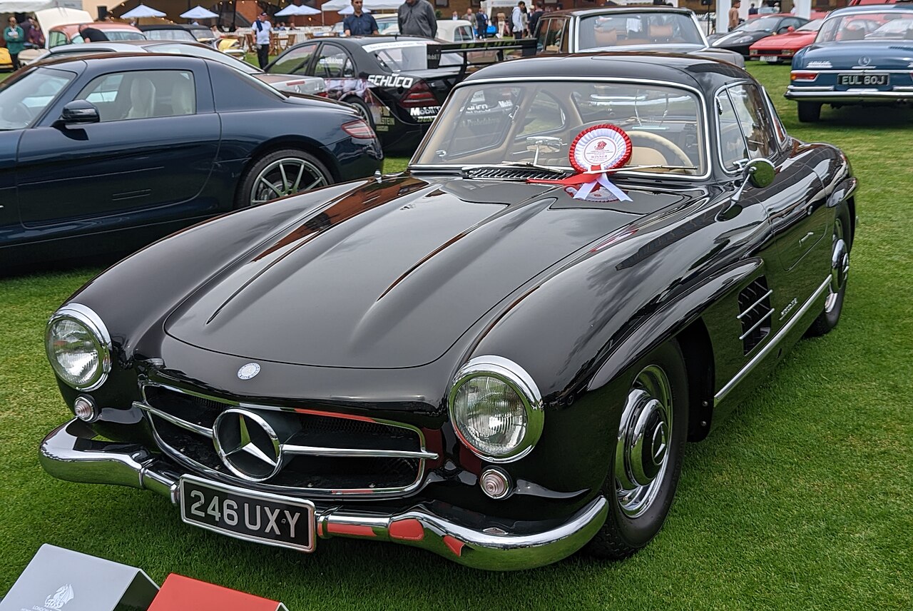 Black 1955 Mercedes-Benz 300 SL Gullwing with a show rosette at the base of the windscreen, front left three-quarter view on a lawn.