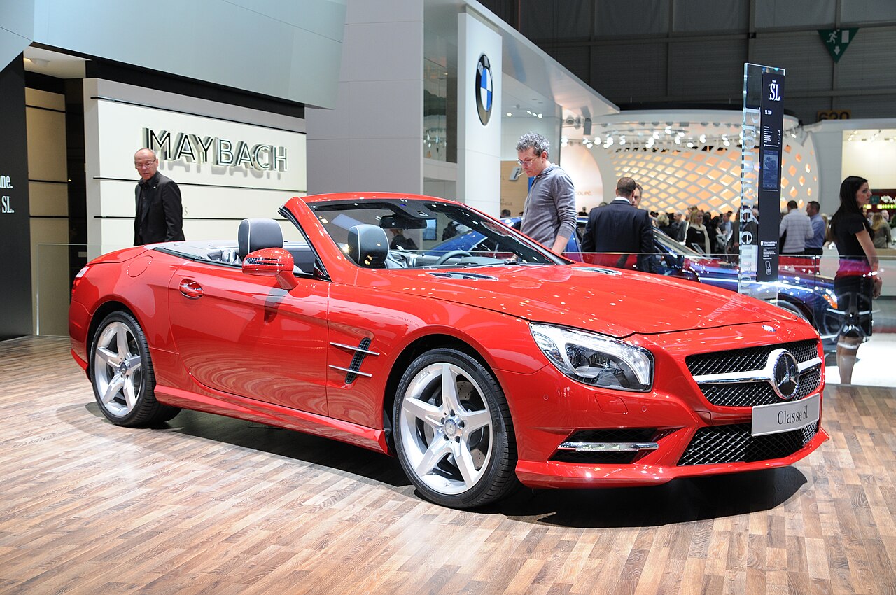 Red Mercedes-Benz SL roadster with its roof down, front right three-quarter view on a wooden floor at a motor show.
