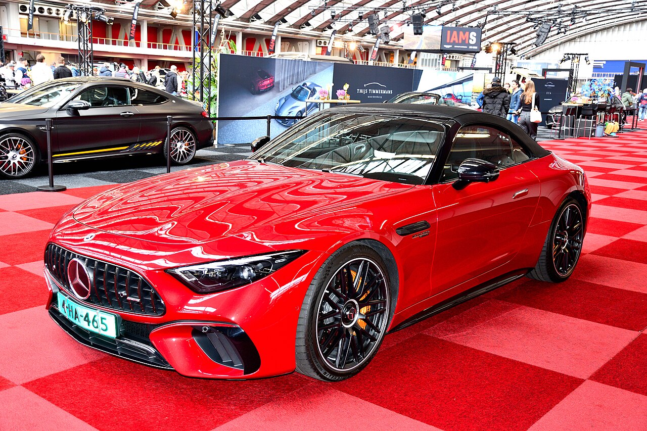 Red Mercedes-Benz SL (R232) with its black soft top up, front three-quarter view on a chequered red carpet at the Amsterdam Motor Show.