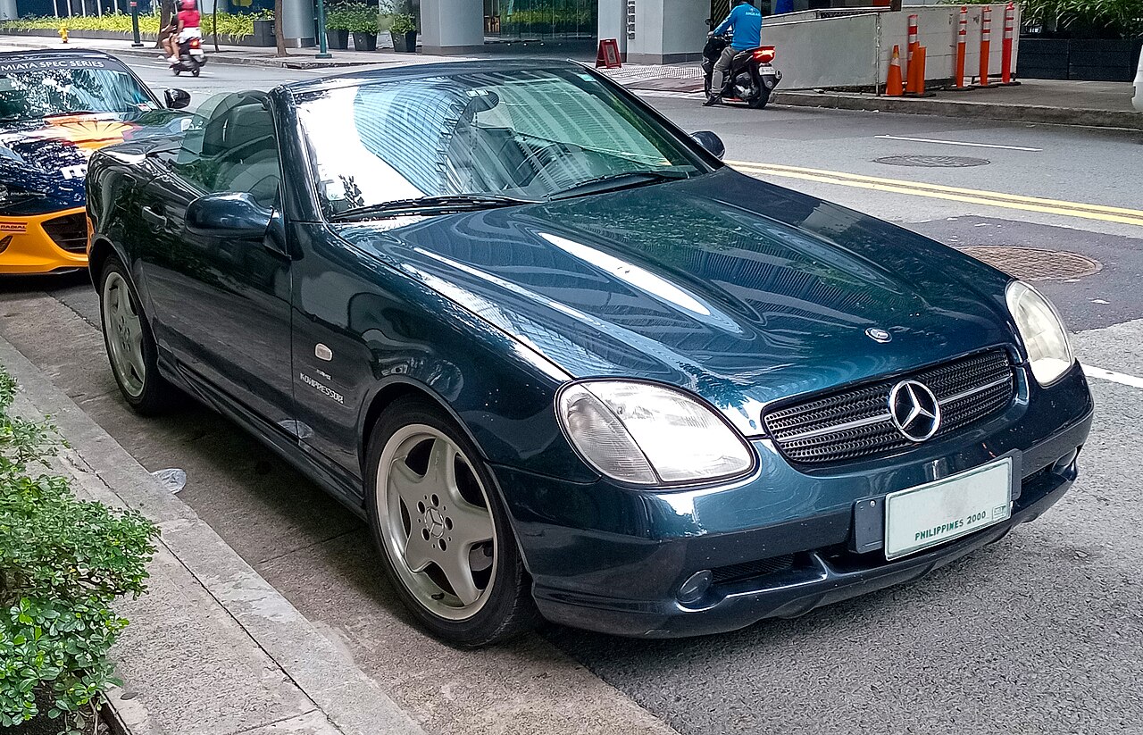 1997 Mercedes-Benz R170 SLK 230 Kompressor in dark green with its roof down, front three-quarter view parked on a city street.