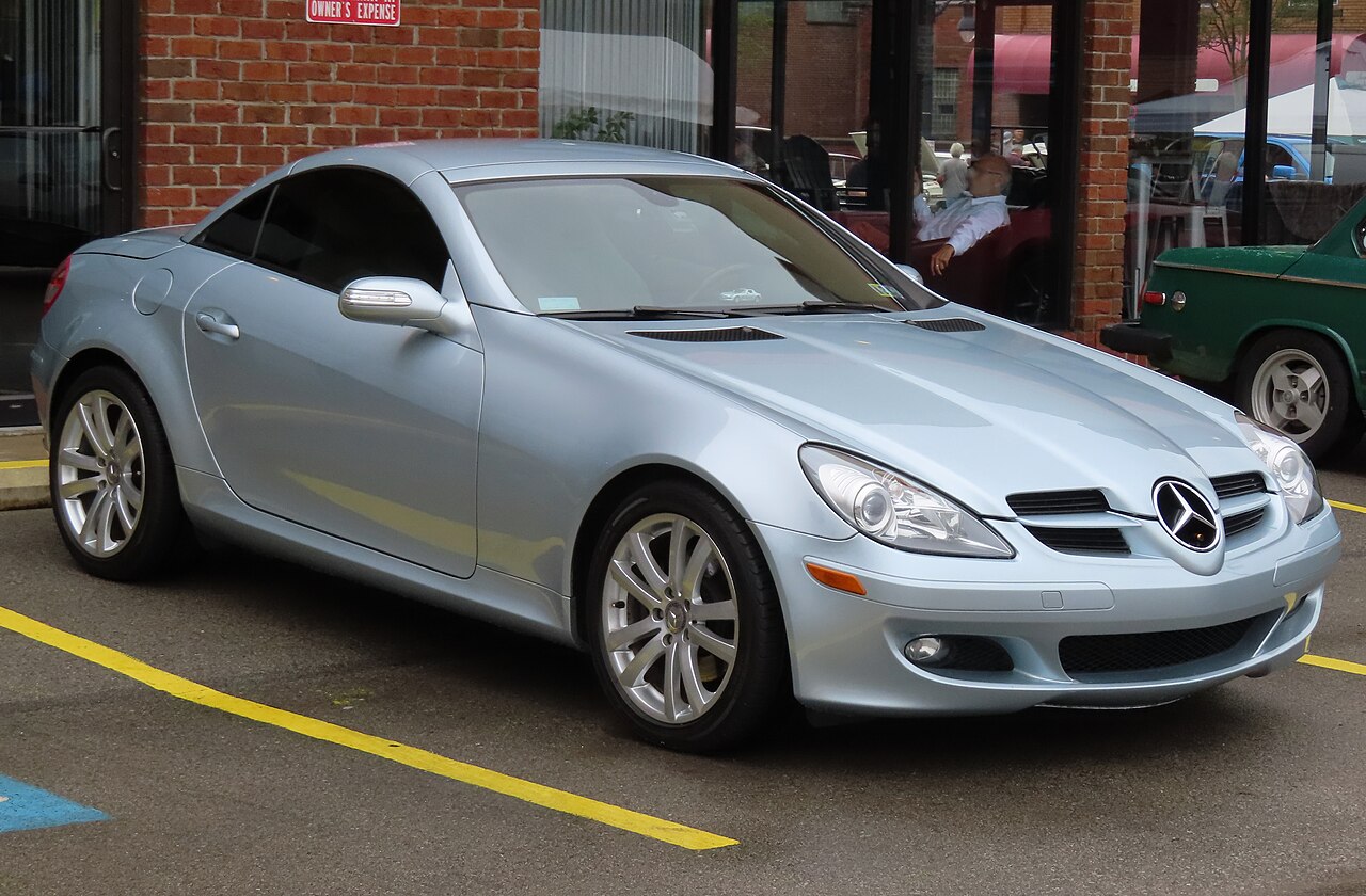 Pale silver-blue 2007 Mercedes-Benz SLK 280 with its roof up, front right three-quarter view in a car park by a brick building.