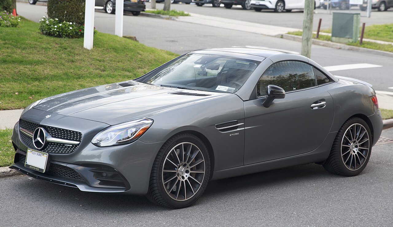 Grey 2017 Mercedes-AMG SLC 43 with its roof up, front left three-quarter view parked on a street beside a lawn.