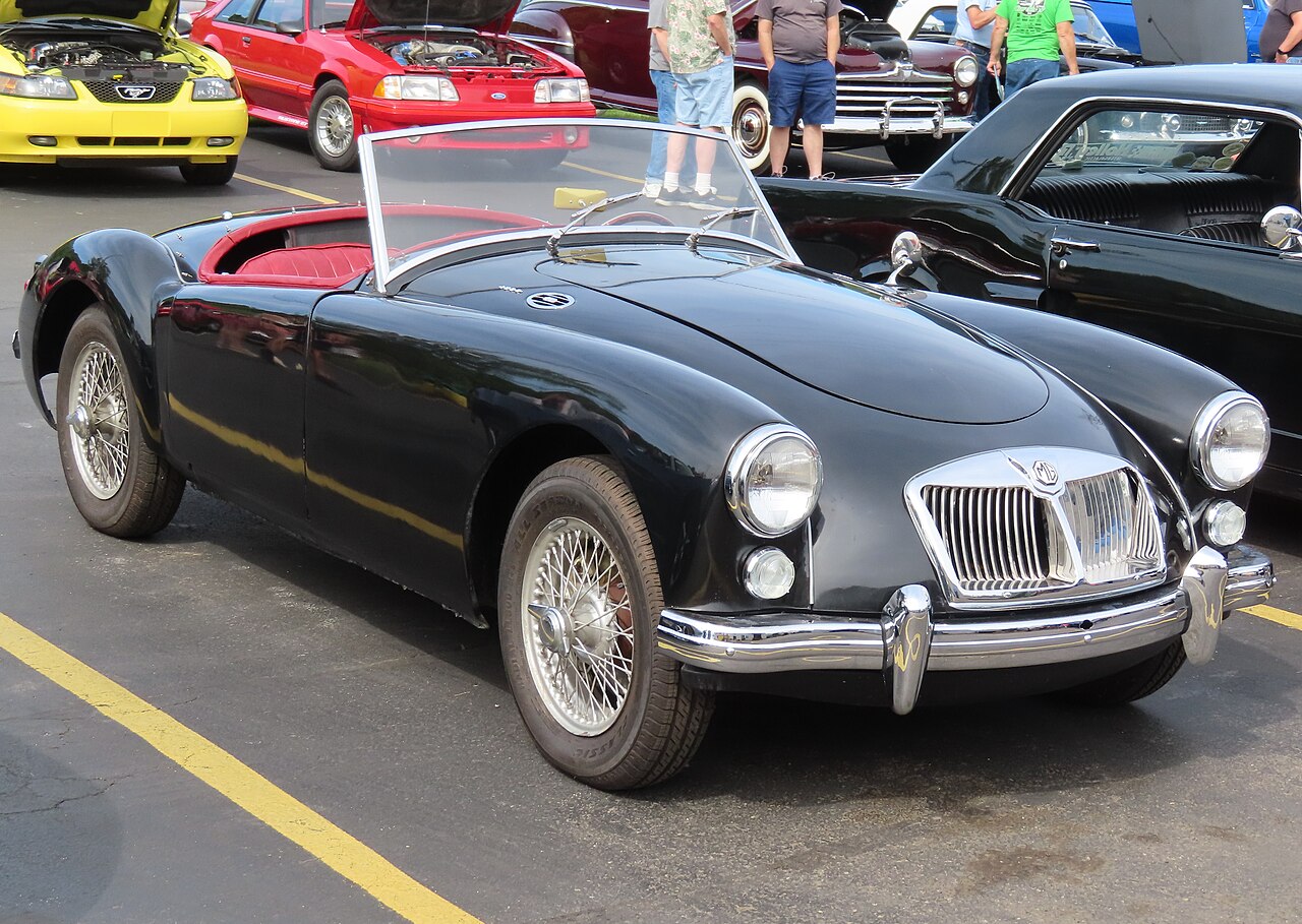 Black 1960 MGA 1600 roadster with red seats and wire wheels, front three-quarter view in a car park at a show.