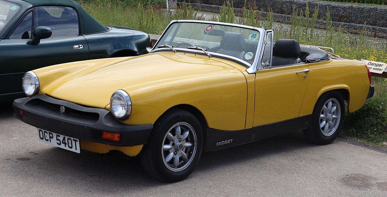 Yellow 1978 MG Midget 1500 with black bumpers and alloy wheels, roof down, front left three-quarter view on tarmac.