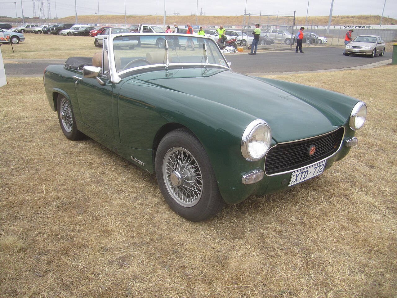 Dark green 1969 MG Midget Mk III roadster with wire wheels and its roof down, front three-quarter view on dry grass.