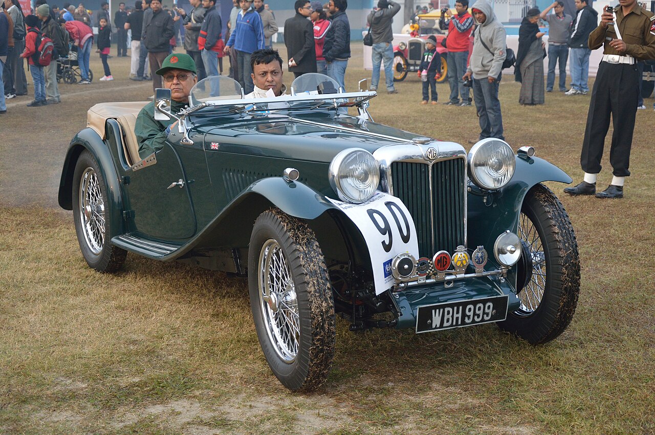 1946 MG TC roadster in dark green with wire wheels and two people aboard, front right view on grass at a Kolkata vintage car rally.