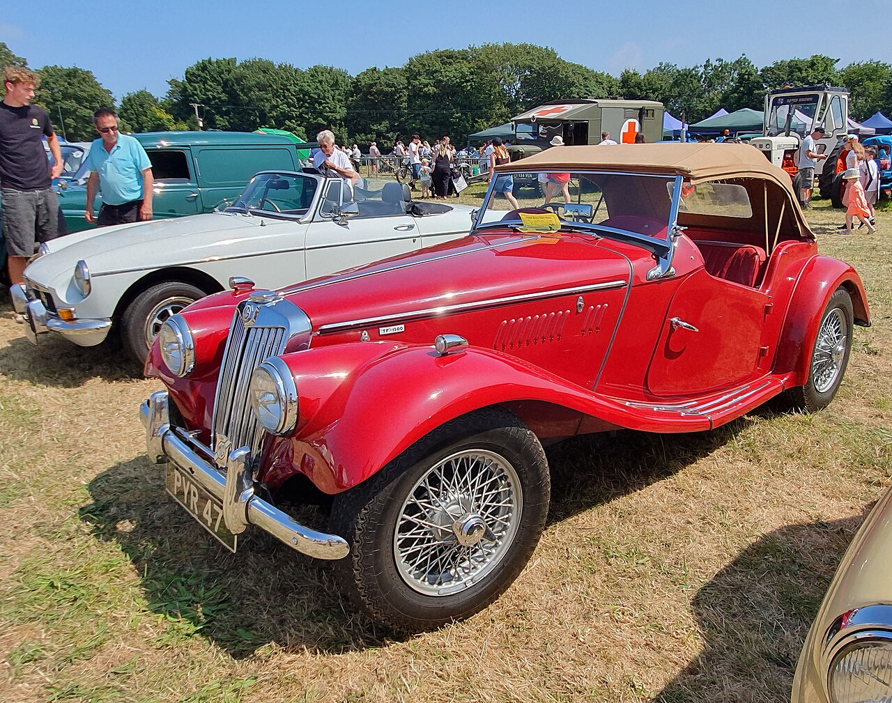 Red MG TF 1500 roadster with its tan hood up, front left three-quarter view on grass at a classic car show in Cornwall.