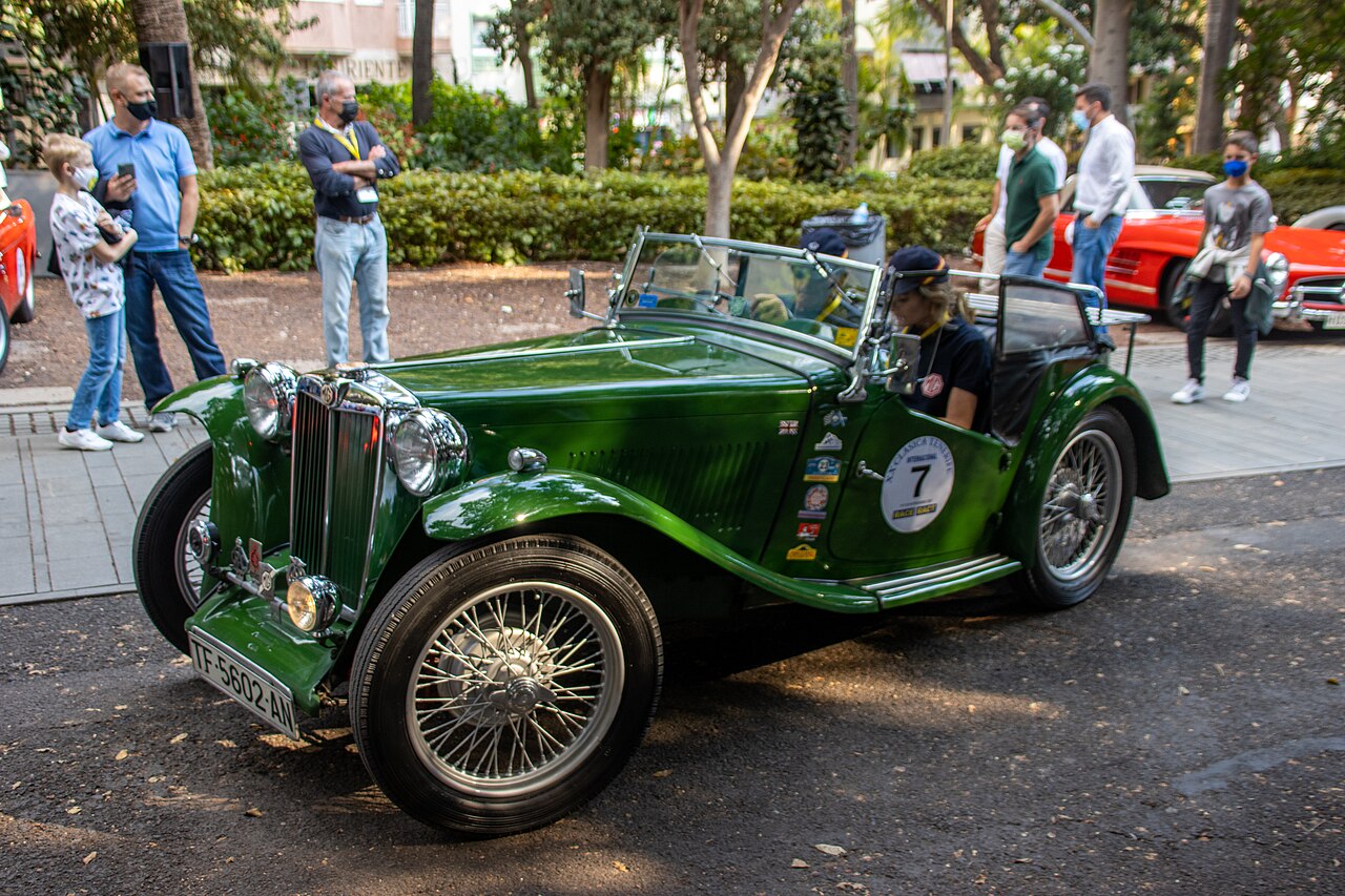 Green MG T-series roadster with wire wheels and two people aboard, front left view on a street during a classic car event in Tenerife.
