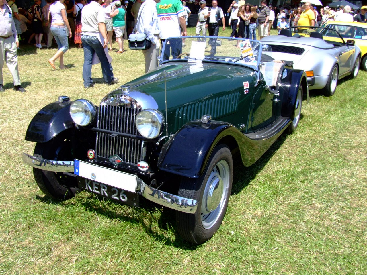 1952 Morgan Plus 4 in dark green with black wings and its roof down, front left three-quarter view on grass at a crowded show.
