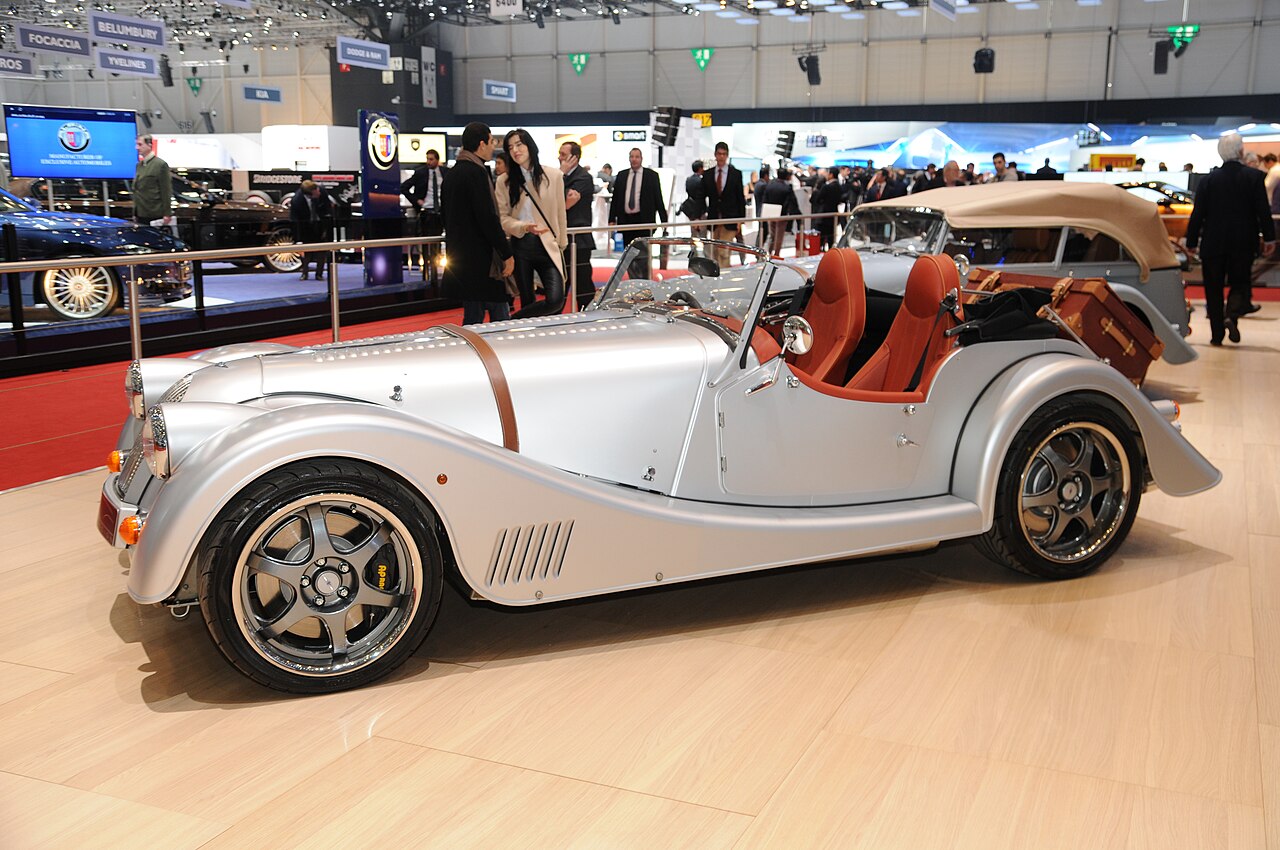 Silver Morgan roadster with a leather bonnet strap and a leather trunk on the rear rack, side-on at the 2013 Geneva Motor Show.
