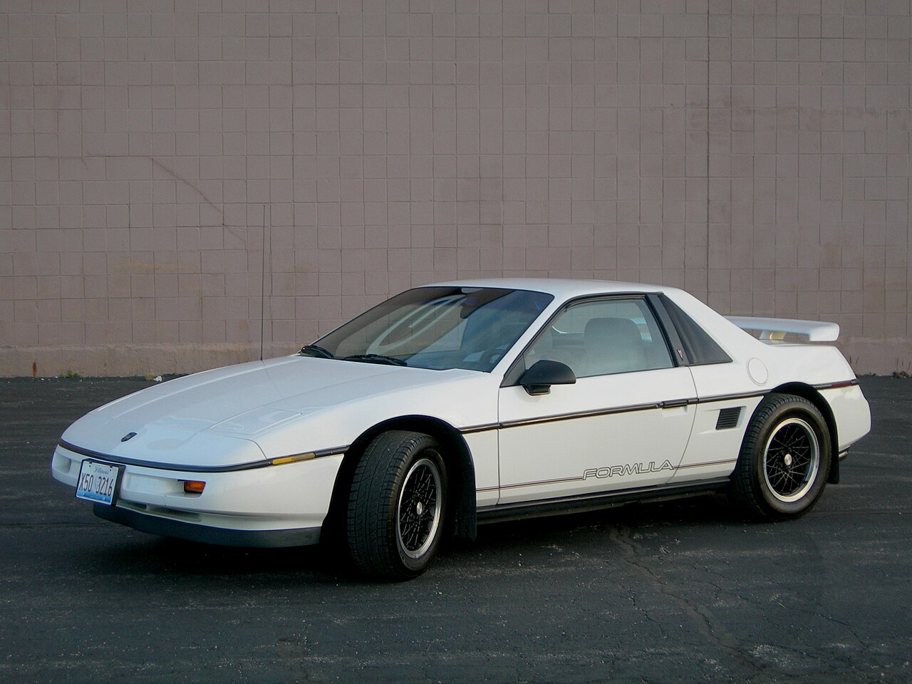 White 1988 Pontiac Fiero Formula with black mesh wheels, front left three-quarter view against a plain tiled wall.