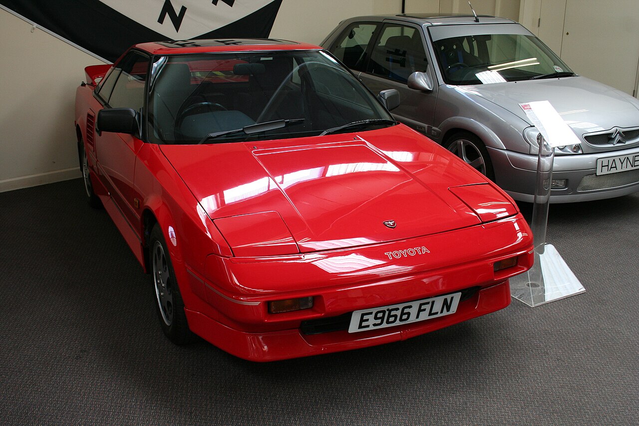 Red Toyota MR2 AW11, front right three-quarter view on the floor of a motor museum.