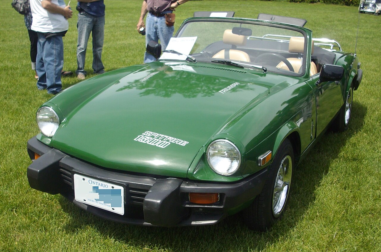 Green 1980 Triumph Spitfire 1500 with its roof down, front three-quarter view on grass at a British car show.
