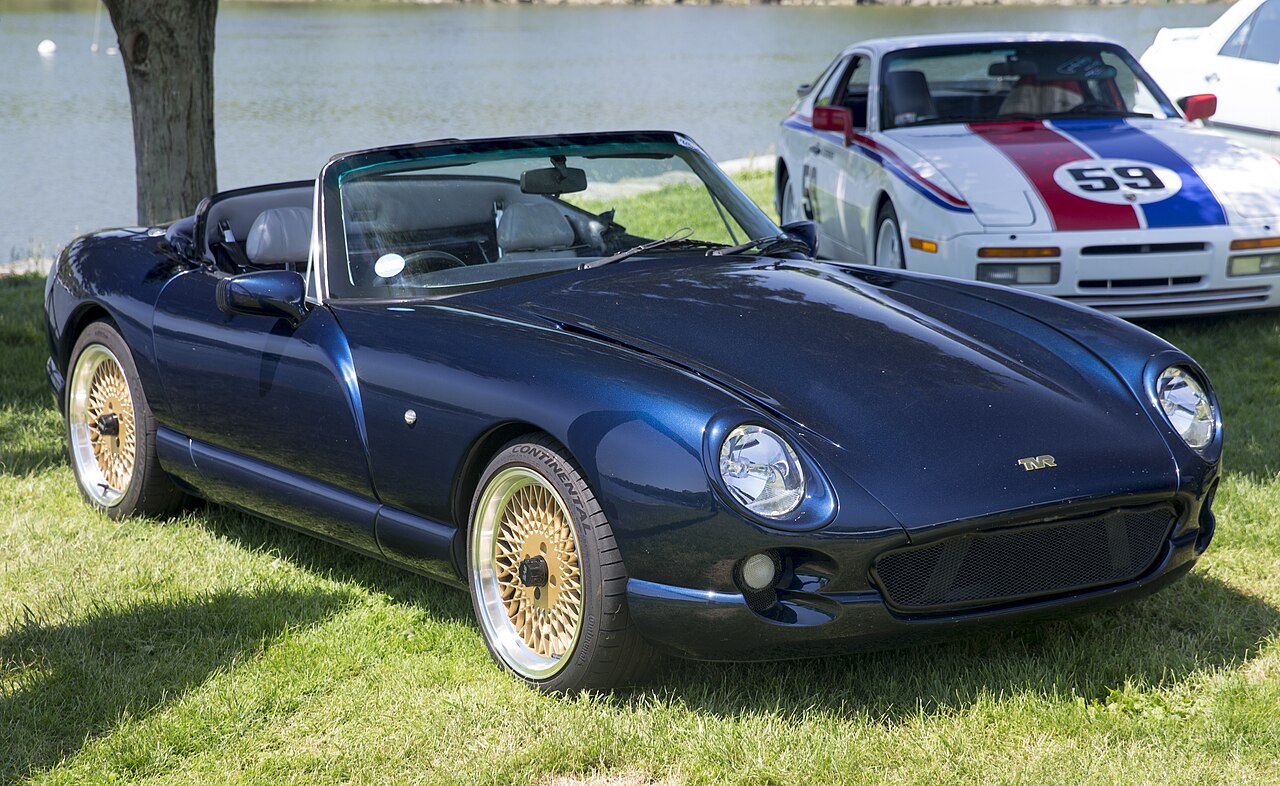 1994 TVR Chimaera 400 in dark blue with gold mesh wheels and its roof down, front right three-quarter view on grass beside the water.