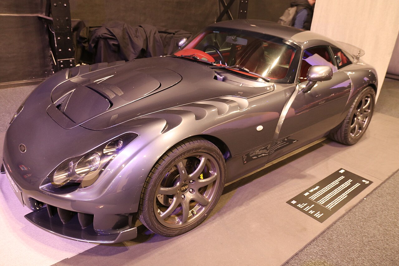 2005 TVR Sagaris in grey with a vented bonnet and red interior, front three-quarter view on an indoor show stand.