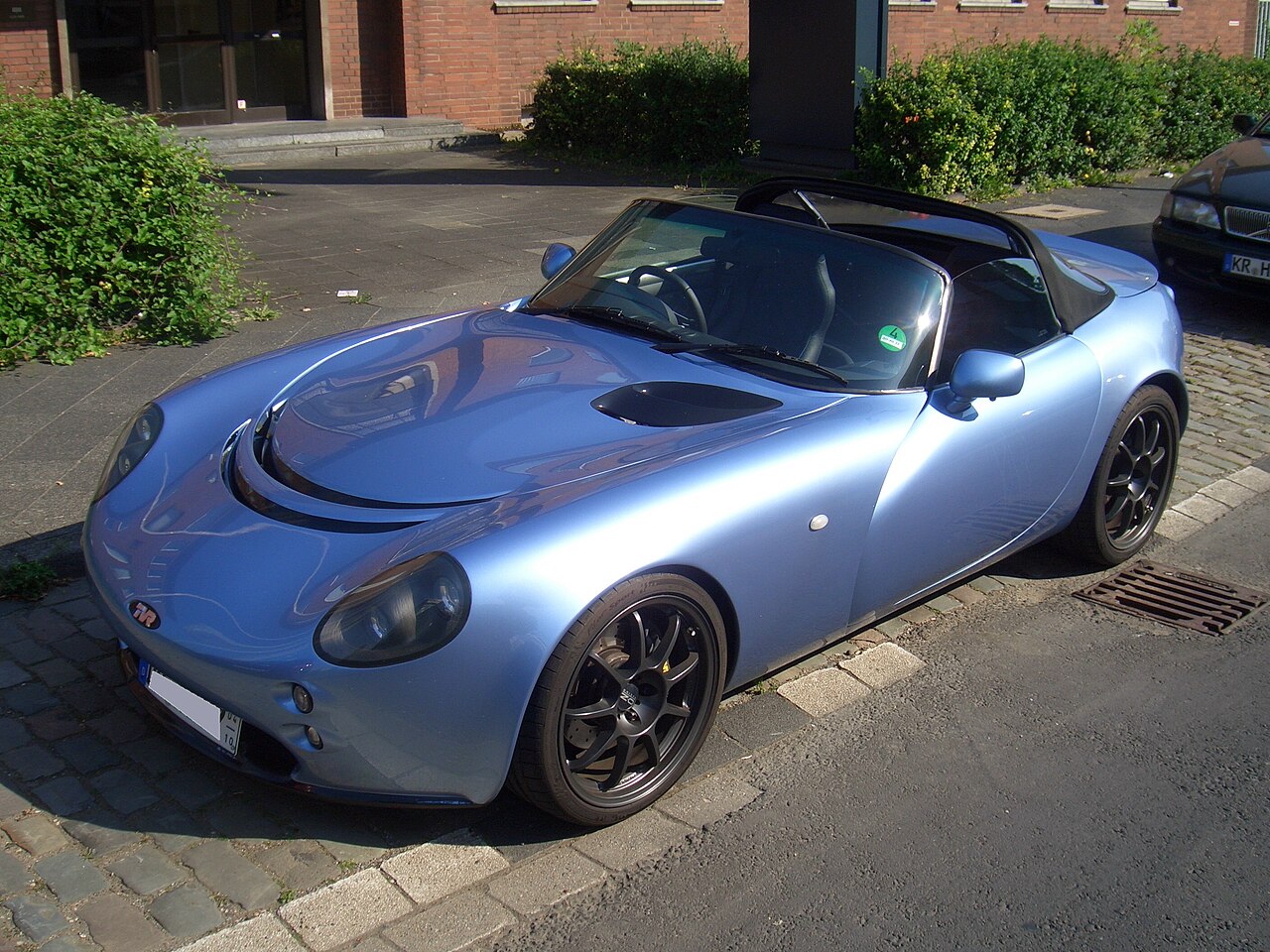 Light blue TVR Tamora roadster with its roof down and black alloy wheels, front three-quarter view parked on a city street.